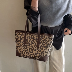 Detail of large leopard print tote bag with brown leather handles worn by a model