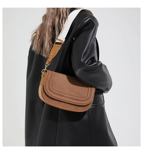 Detail of brown suede shoulder bag with wide white fabric strap on leather jacket