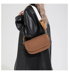Close-up of brown saddle crossbody bag with wide woven strap on a leather coat model