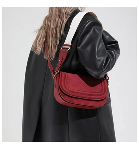 Red flap saddle bag with wide woven strap shown on model in a minimalist setting