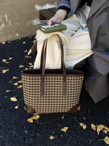 Close-up of brown houndstooth tote bag with leather trim and handle on outdoor wooden bench