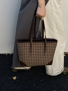 Close-up of a large houndstooth tote bag with dark brown leather handles and vintage trim