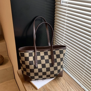 Detail of checkered canvas tote bag with premium dark brown leather handles and stitching