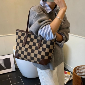 Close-up of brown checkerboard tote bag with durable leather straps and reinforced corners