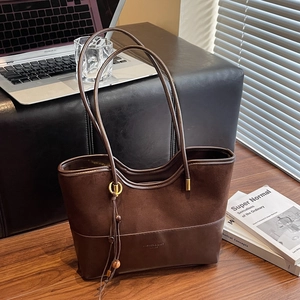 Vintage dark brown leather tote bag with tassel charm on a wooden desk setting