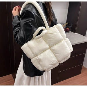 Side view of a large white quilted puffer tote bag worn by a model in a modern interior