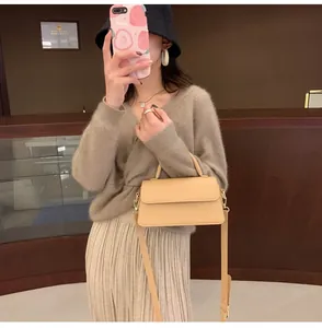 Detail of a beige rectangular handbag with top handle and gold-tone buckle on model
