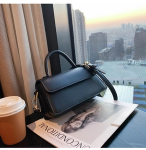 Detail shot of black leather handbag with gold hardware against a sunset city backdrop