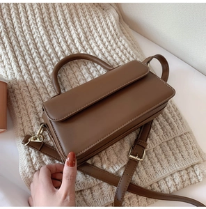 Close-up of brown leather handbag with gold metal clasp on a soft knit fabric