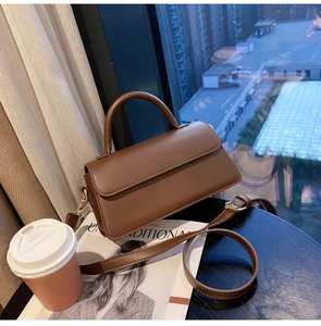 Detail of vintage brown leather handbag on a wooden table next to a coffee cup