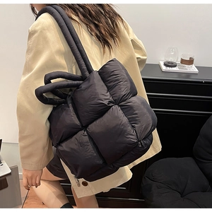 Quilted black puffer tote bag shown on shoulder in a minimalist indoor setting