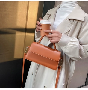 Close-up of stylish orange leather crossbody handbag worn with a chic beige trench coat
