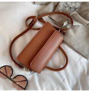 Flat lay of brown vintage crossbody bag on white fabric with fashion accessories