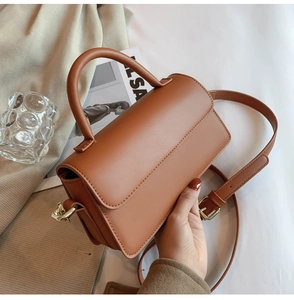 Detail of a brown leather bag showing a round handle and light gold metal buckles