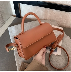 Detailed view of caramel leather handbag featuring gold hardware and a curved top handle