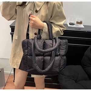 Detail of black quilted puffer tote bag with puffy straps held by model in trench coat