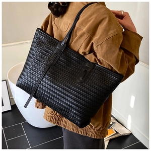 Détail de la texture tressée et des anses du sac cabas noir porté par un mannequin