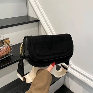 Minimalist black saddle bag with suede flap and cream wide strap in a modern indoor setting