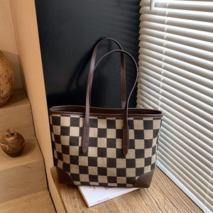 Checkerboard patterned tote bag with brown leather handles on a natural wooden table