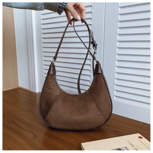 Detail of brown suede crescent bag with leather trim and adjustable strap in cozy setting