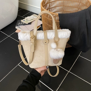 Beige bucket bag with white faux fur trim and pom-pom charm shown in hand