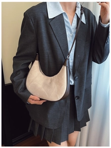 Close-up of a beige suede crescent bag with dark brown leather trim on a model