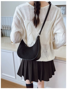 Detail of black crescent shoulder bag with mixed leather texture on white knit sweater