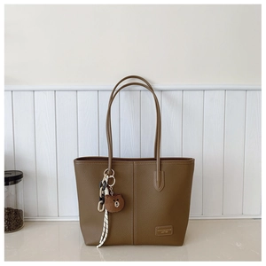 Detail of brown litchi textured tote bag with metal logo and bear charm accessory