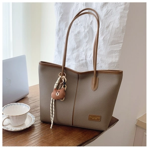 Detail view of khaki tote bag with brown bear charm on a desk with a laptop