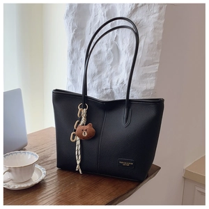 Black lychee textured tote bag with a brown bear plush charm on a wooden table surface