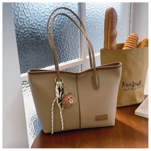 Detail of khaki pebbled leather tote bag with brown bear charm and metal logo badge