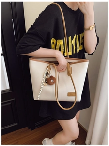 Detail of white lychee leather tote bag featuring brown straps, bear charm, and silk scarf