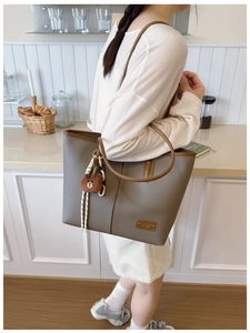 Detail of taupe leather tote bag with brown bear pendant shown on model's shoulder