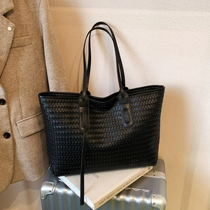 Sac cabas en cuir tressé noir avec de longues anses posé sur une valise