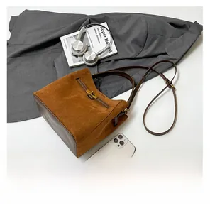 Détail du sac seau en daim marron avec fermoir tournant doré et finitions en cuir