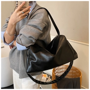 Detail of a large black soft leather tote bag with wide shoulder strap on a female model