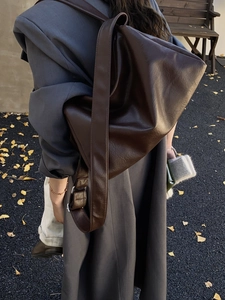 Detail view of large dark brown tote bag with glossy leather texture and wide strap