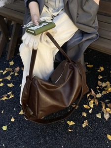 Deep brown tote bag detail with smooth leather texture and metallic zipper on autumn leaves