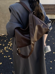 Close-up of deep brown large hobo bag with wide strap on grey coat in autumn