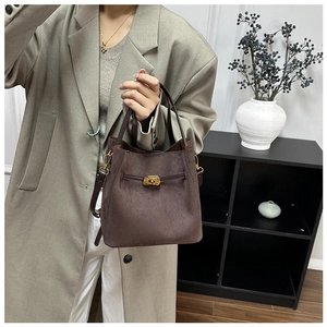 Sac seau en daim marron porté par un mannequin en manteau gris au décor moderne