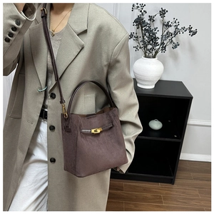 Sac seau en daim marron avec poignée en cuir et fermoir doré porté par un mannequin