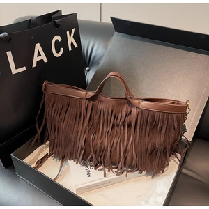 Détail d'un sac à main marron à franges avec anses en cuir et pompons en daim en boîte