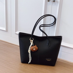 Minimalist black tote bag with lychee grain leather and cute bear charm in indoor setting