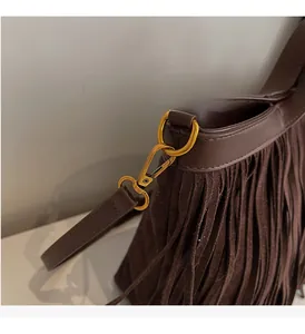 Détail de sac bandoulière en daim marron avec boucles dorées et pompons bohèmes