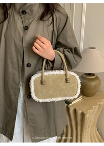 Detail einer beigen Plüschtasche mit Pelzbesatz und runden Griffen auf einem Tisch