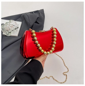 Detail of red glossy acrylic clutch with gold beaded handle and metal chain strap