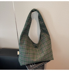 Detail of green plaid hobo bag with texture fabric and black button closure on a book