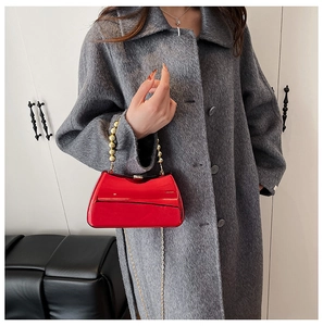 Detail of red patent leather handbag with gold bead handle on grey textured coat