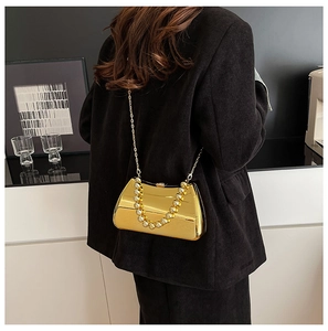 Close-up of a glossy gold metal evening clutch with beaded handle and chain strap on a model