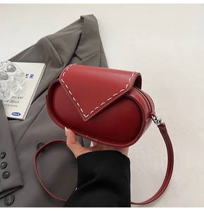 Detail of red leather crossbody bag with white stitching and triangular flap design